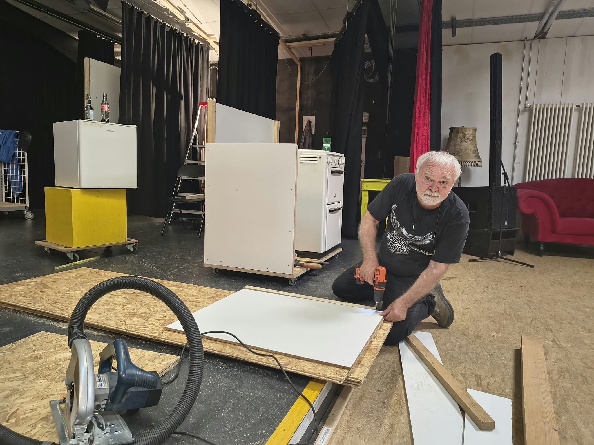 Ein Mitglied kniet auf der Bühne und befestigt mit einem Akkuschrauber eine weiße Platte auf einem Holzbauteil.