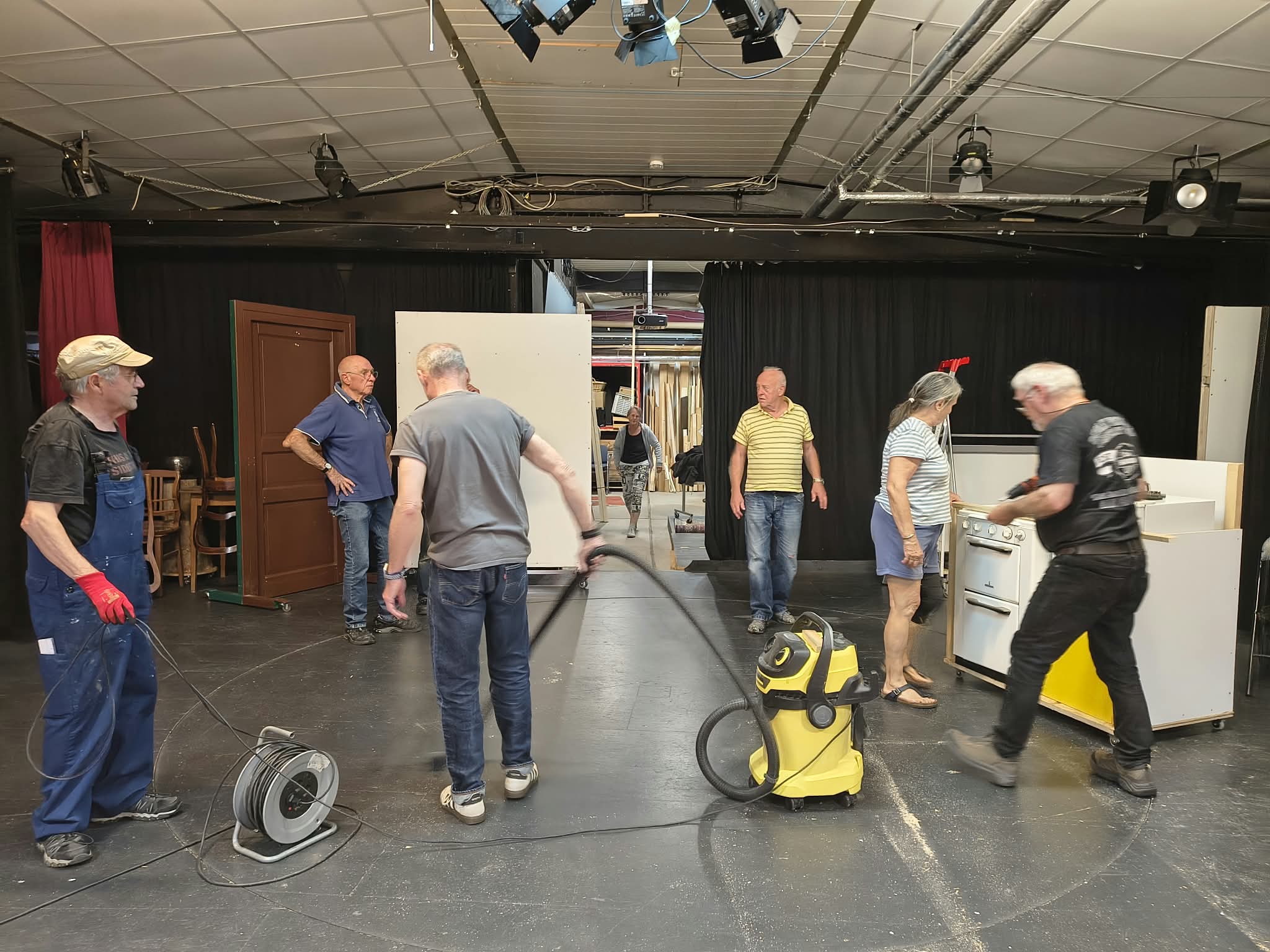 Mehrere BAC-Mitglieder arbeiten zwischen Kulissenwänden, Werkzeugen und einem Staubsauger auf der Bühne.