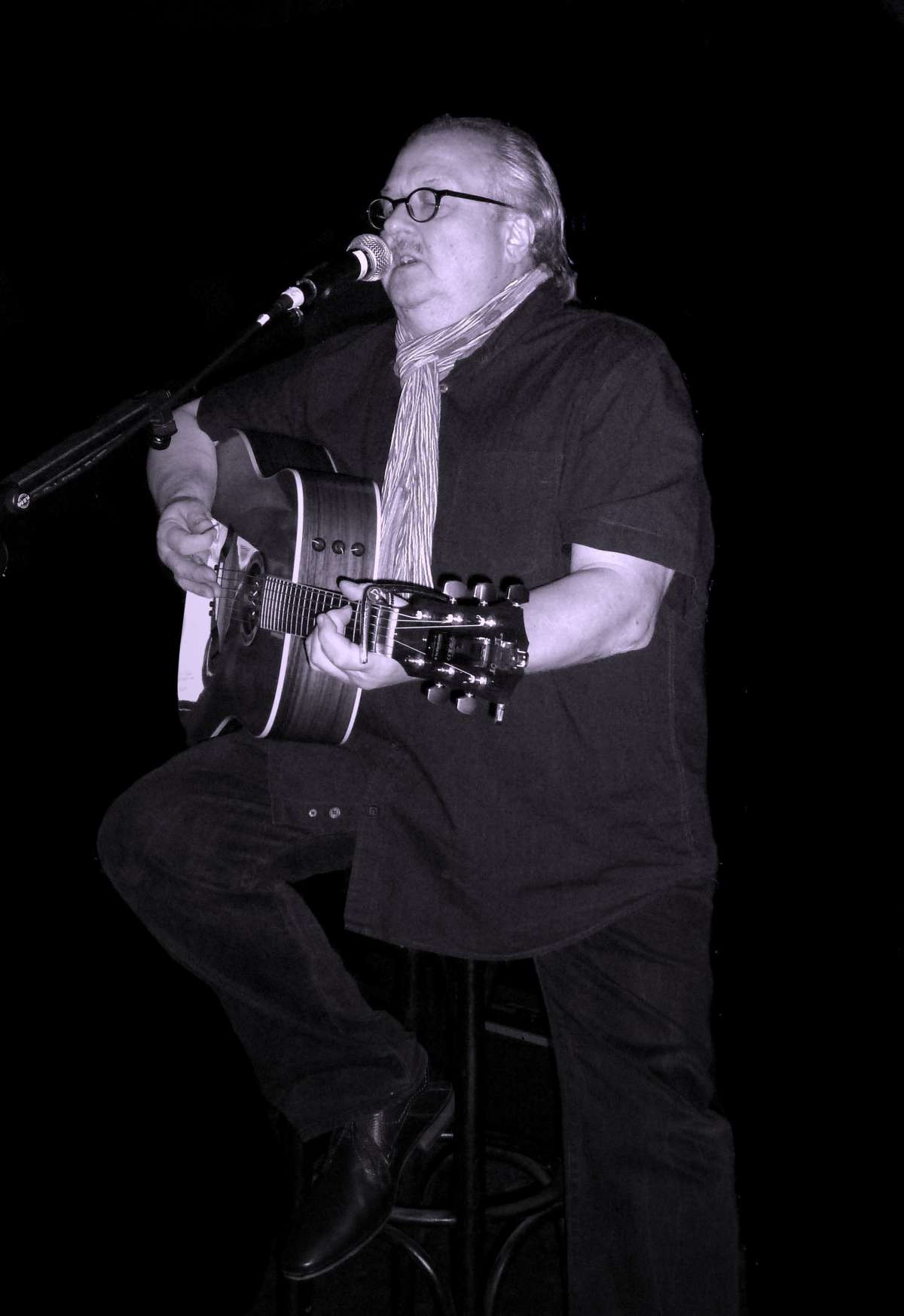 Lobo Andersson singt am Mikrofon und spielt akustische Gitarre, Schwarz-Weiß-Foto.